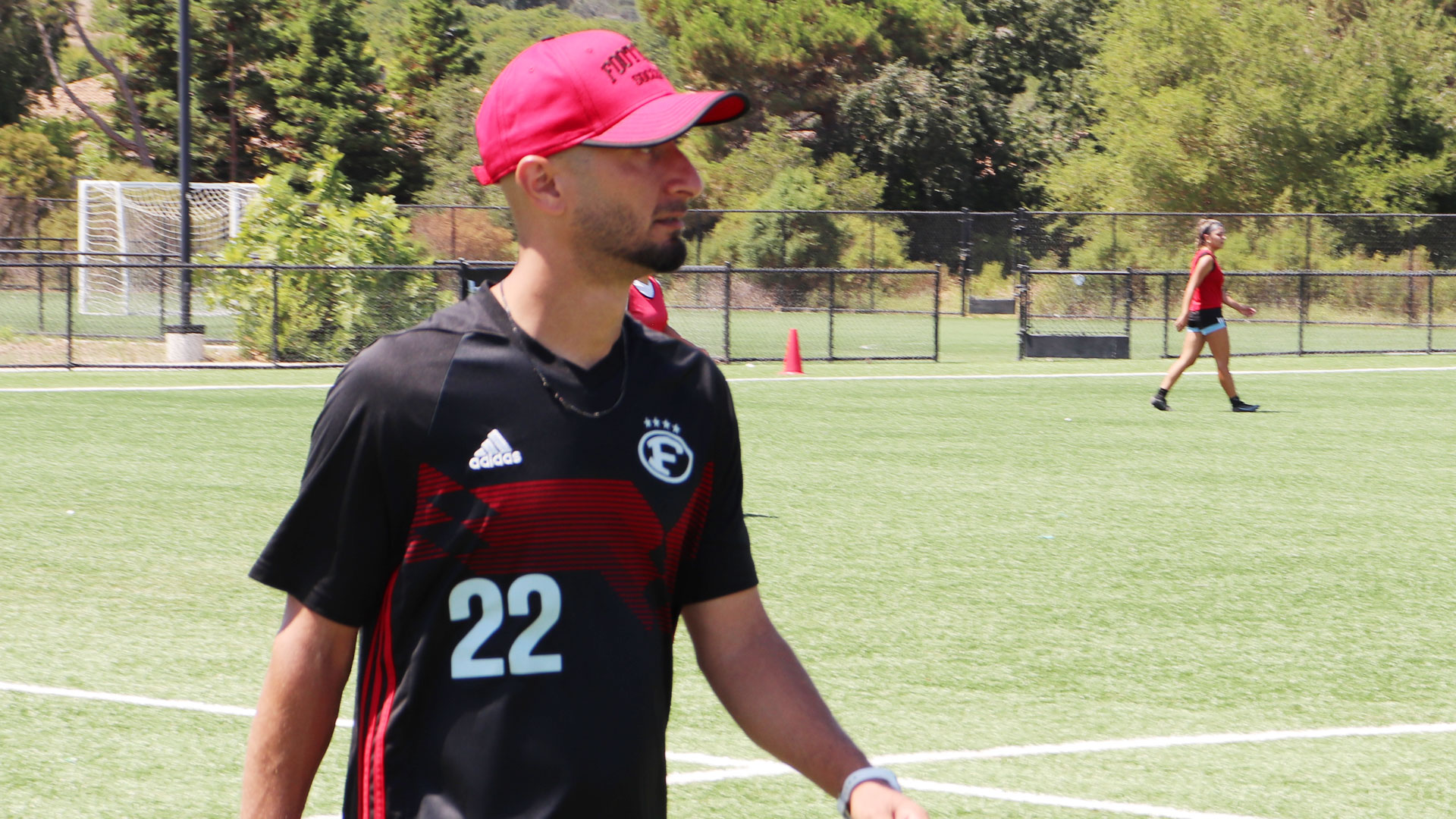 coach in black tshirt and red cap walking on pitch